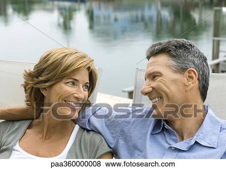 Mature couple sitting near water, smiling at each other View Large Photo Image Stock Photo - Mature couple sitting near water, smiling at each other. Fotosearch