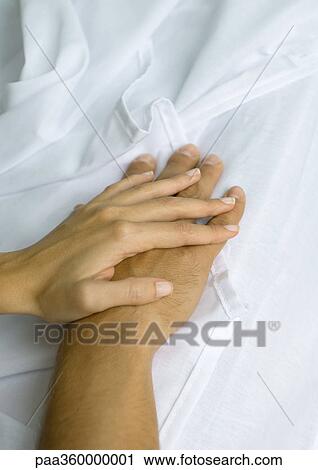 Stock Image - Woman's hand on top of man's, on sheets. Fotosearch