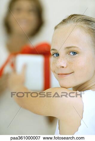 Stock Photo - Girl holding out present to woman, smiling over shoulder at camera. Fotosearch