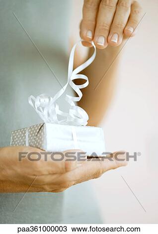 Stock Image - Man handing woman gift, close-up of hands. Fotosearch