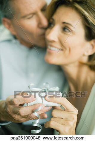 Mature couple with present, man kissing woman's cheek View Large Photo Image Stock Photo - Mature couple with present, man kissing woman's cheek. Fotosearch