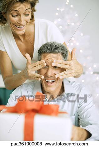 Woman surprising husband with christmas present View Large Photo Image Stock Photo - Woman surprising husband with christmas present. Fotosearch