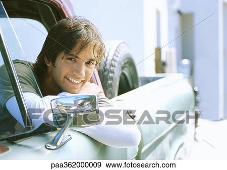 Stock Photo - Young man in car, leaning on edge of car window frame. Fotosearch