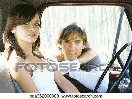 Stock Photo - Young woman in car, man leaning on edge of car window frame. Fotosearch