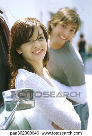 Young woman leaning against truck, man making face behind her View Large Photo Image Stock Photograph - Young woman leaning against truck, man making face behind her. Fotosearch