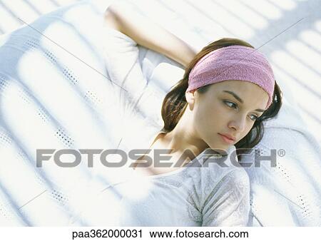 Stock Image - Young woman lying in shade, looking pensive. Fotosearch