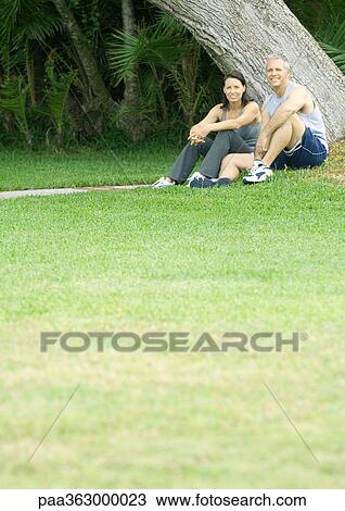 Stock Image - Couple in workout clothes sitting next to tree. Fotosearch