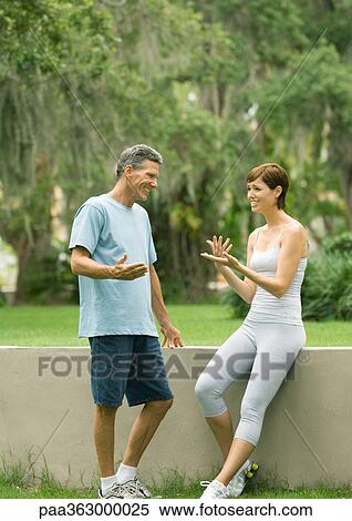 Stock Photography - Couple in workout clothes talking next to low wall. Fotosearch
