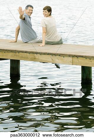 Couple sitting on dock, man waving at camera View Large Photo Image Stock Image - Couple sitting on dock, man waving at camera. Fotosearch