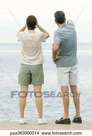 Couple standing by edge of water, looking at view View Large Photo Image Picture - Couple standing by edge of water, looking at view. Fotosearch