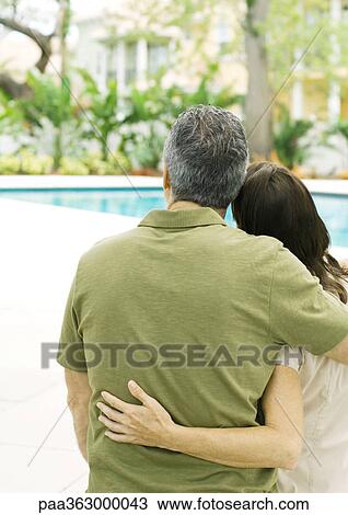 Couple standing with arms around each other, looking at swimming pool View Large Photo Image Stock Image - Couple standing with arms around each other, looking at swimming pool. Fotosearch