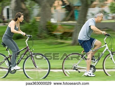Stock Photo - Mature couple riding bikes, side view. Fotosearch