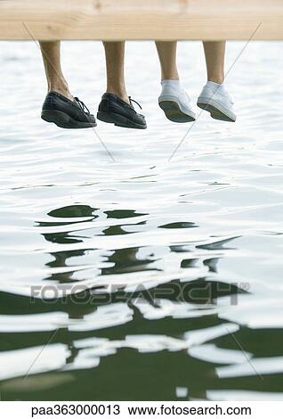 Stock Image - Two people sitting on dock, view of feet. Fotosearch