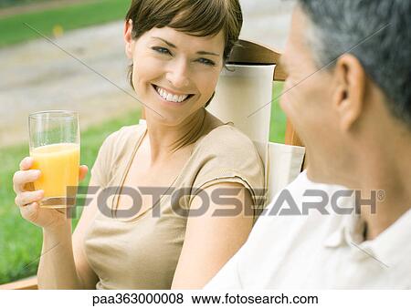 Woman holding glass of orange juice, looking at husband View Large Photo Image Stock Photo - Woman holding glass of orange juice, looking at husband. Fotosearch