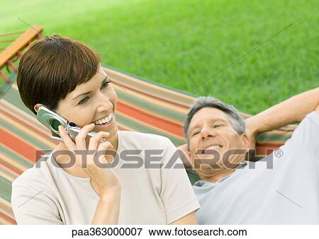 Stock Photo - Woman using cell phone while man lounges on hammock. Fotosearch