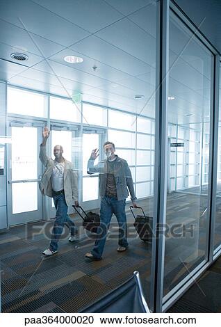 Stock Image - Travelers with suitcases waving in airport. Fotosearch