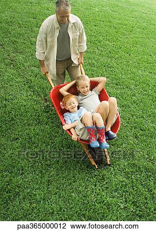 Father pushing two children in wheelbarrow View Large Photo Image Stock Image - Father pushing two children in wheelbarrow. Fotosearch