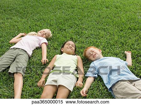 Three children lying in grass View Large Photo Image Stock Photography - Three children lying in grass. Fotosearch