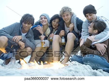 Group of young adult friends sitting around campfire View Large Photo Image Stock Photo - Group of young adult friends sitting around campfire. Fotosearch