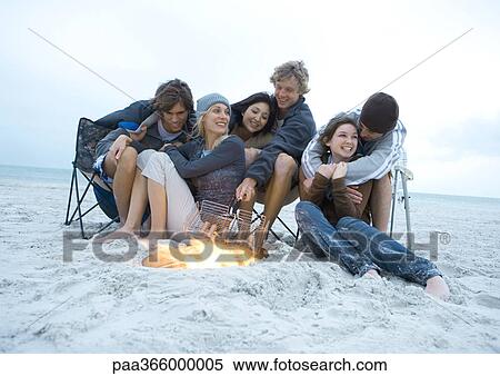 Stock Photography - Group of young friends sitting next to campfire on beach. Fotosearch