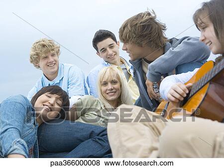 Stock Photo - Group of young people hanging out, one playing guitar. Fotosearch