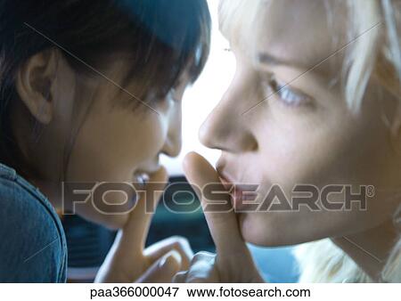 Stock Photo - Two young women holding fingers to lips. Fotosearch
