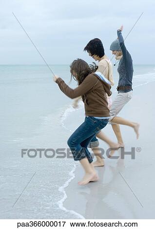 Stock Photo - Young adult friends jumping into surf on beach. Fotosearch