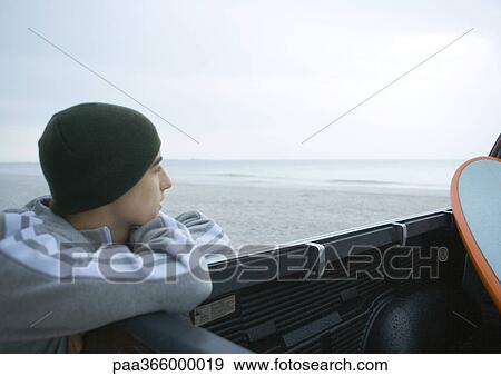 Stock Photo - Young man leaning on edge of pickup truck on beach. Fotosearch
