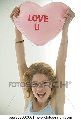 Stock Image - Preteen girl holding up heart shaped pillow. Fotosearch