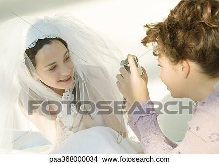Picture - Preteen girl taking photo of friend dressed in wedding dress. Fotosearch