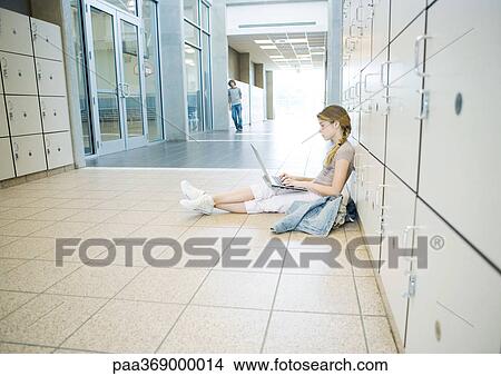 Teenage girl sitting on floor, leaning against lockers, using laptop, teenage boy standing in distance View Large Photo Image Picture - Teenage girl sitting on floor, leaning against lockers, using laptop, teenage boy standing in distance. Fotosearch