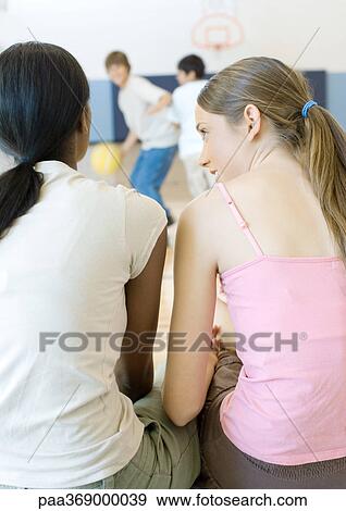 Two teen girls sitting and talking while teen boys play basketball in background View Large Photo Image Stock Photo - Two teen girls sitting and talking while teen boys play basketball in background. Fotosearch