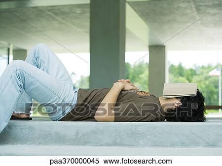 Stock Photography - Male college student lying on ground with book covering face. Fotosearch