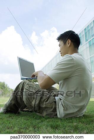 Male college student sitting on grass in campus, using laptop View Large Photo Image Stock Image - Male college student sitting on grass in campus, using laptop. Fotosearch