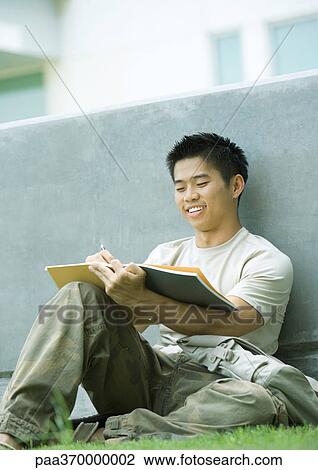 Stock Image - Male college student, sitting on ground, studying. Fotosearch