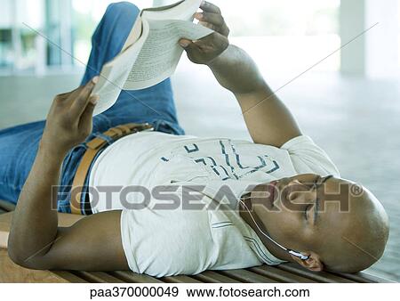 Stock Photo - Man reading book and listening to earphones. Fotosearch