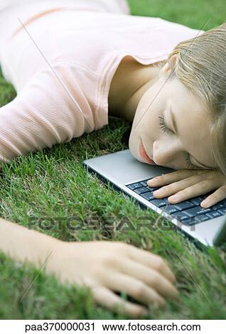 Stock Image - Teenage girl in grass, lying with head on laptop computer. Fotosearch