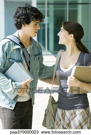 Stock Image - Young couple on college campus, smiling at each other. Fotosearch