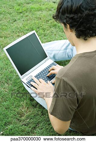 Young man sitting on grass, using laptop computer View Large Photo Image Stock Image - Young man sitting on grass, using laptop computer. Fotosearch