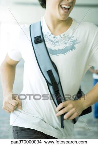 Young man wearing shoulder bag, running, close-up of torso View Large Photo Image Picture - Young man wearing shoulder bag, running, close-up of torso. Fotosearch