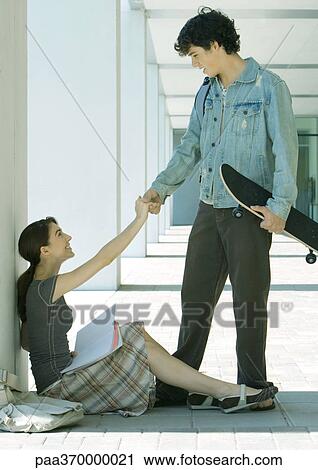 Young man with skateboard reaching hand out to young woman sitting on ground, studying View Large Photo Image Stock Image - Young man with skateboard reaching hand out to young woman sitting on ground, studying. Fotosearch