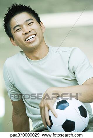 Stock Photo - Young man with soccer ball, smiling. Fotosearch