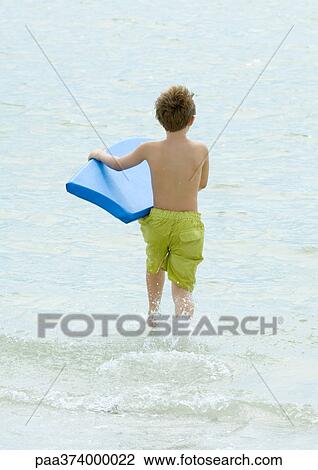 Stock Image - Boy running in surf at beach with body board. Fotosearch