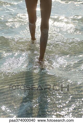 Stock Image - Girl walking through surf, low section. Fotosearch
