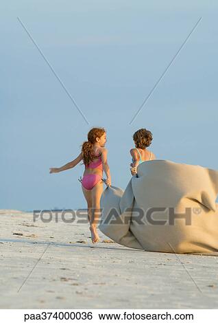 Two girls carrying blanket in wind on beach View Large Photo Image Stock Photograph - Two girls carrying blanket in wind on beach. Fotosearch
