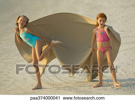 Stock Image - Two girls holding blanket in wind on beach. Fotosearch