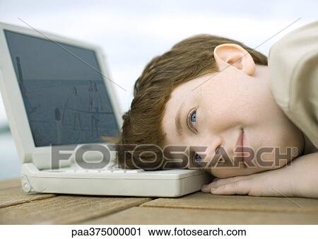 Stock Image - Boy resting head on laptop. Fotosearch