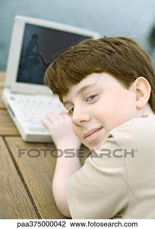 Boy using laptop, looking over shoulder at camera View Large Photo Image Stock Image - Boy using laptop, looking over shoulder at camera. Fotosearch