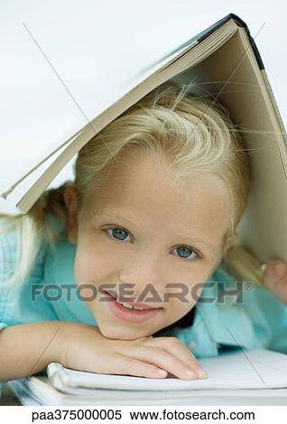 Stock Photography - Girl holding book over head, smiling. Fotosearch