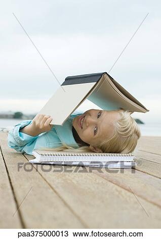 Girl lying on dock with book over head View Large Photo Image Stock Image - Girl lying on dock with book over head. Fotosearch